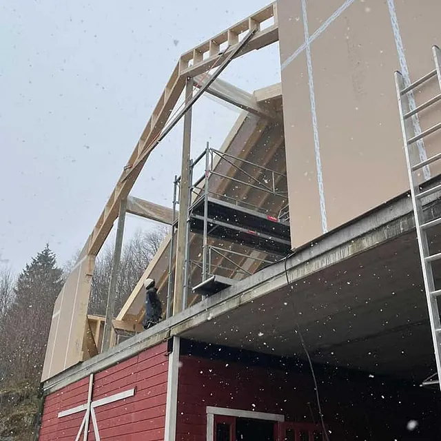 Reisverk og veggelementer settes opp på hus under bygging i snøvær.