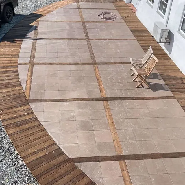 Stor terrasse med fliser og treverk i mønster, enkel stol plassert i solen.
